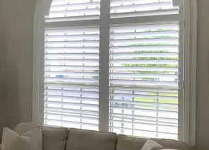 Custom white plantation shutters installed on arched living room window in Alabama home - Beach Blinds window treatments