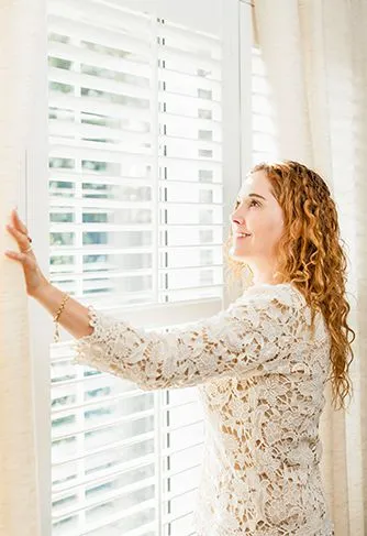 Homeowner adjusting white plantation shutters installed by Beach Blinds in Alabama home