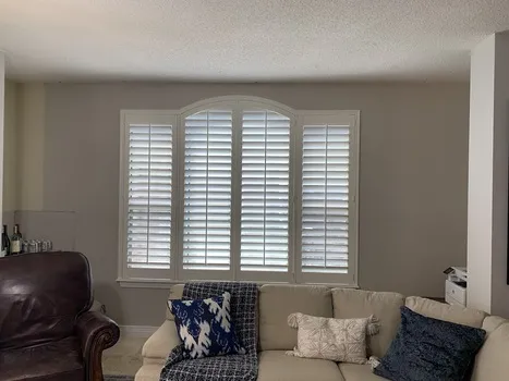 Custom white arched plantation shutters installed in living room window - Beach Blinds Alabama window treatments